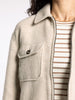 Close-up of a person wearing a light gray coat over a striped shirt on a plain background