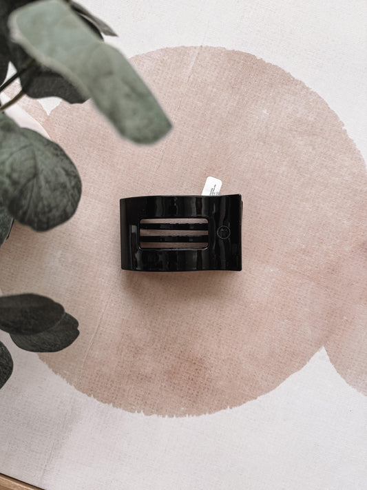 Black rectangular hair clip on a beige circular mat with green leaves in the corner