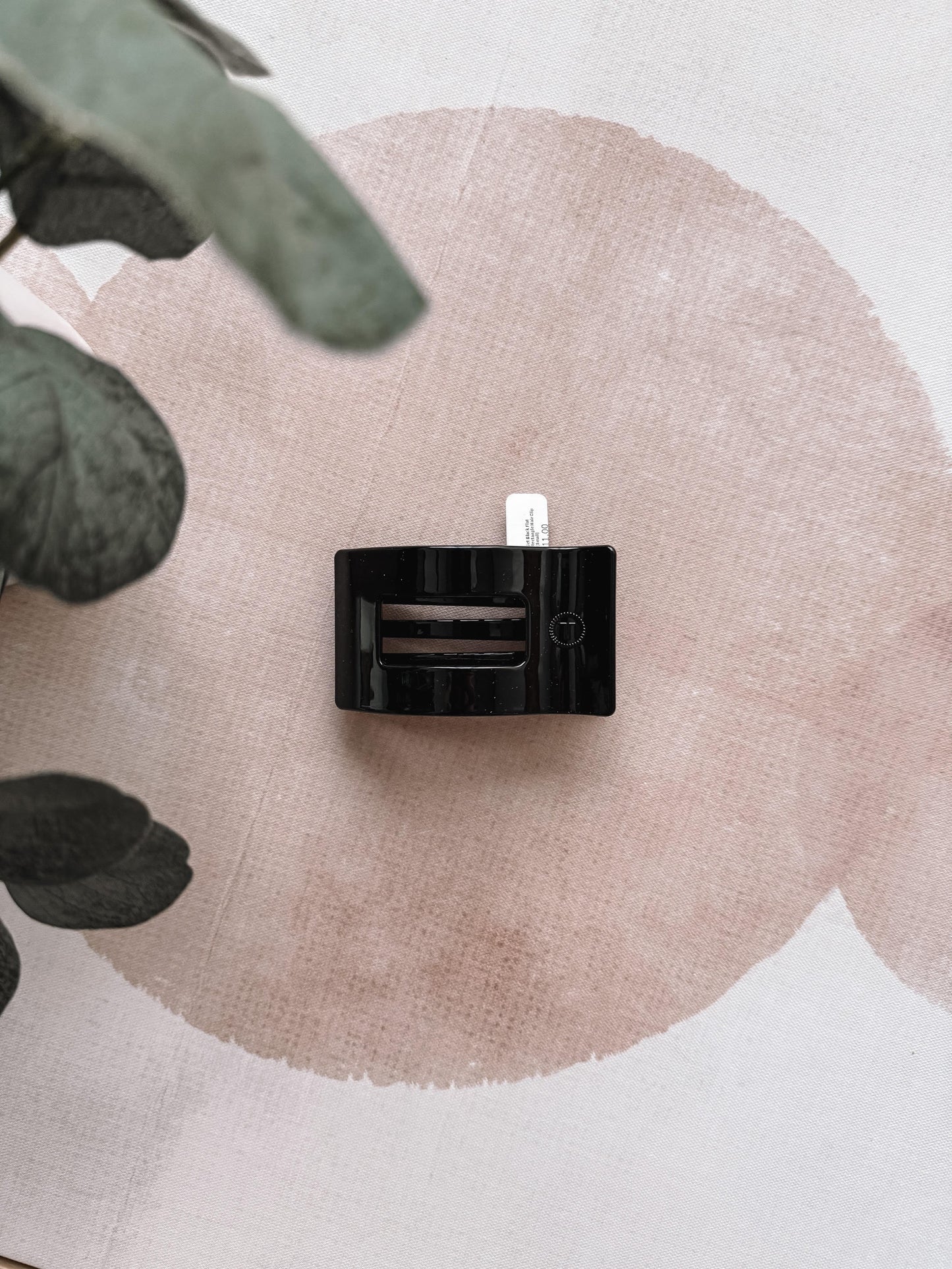 Black hair clip on a textured beige surface with green leaves in the corner
