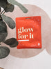 Red package with 'glow for it' text on a light background with leaves.