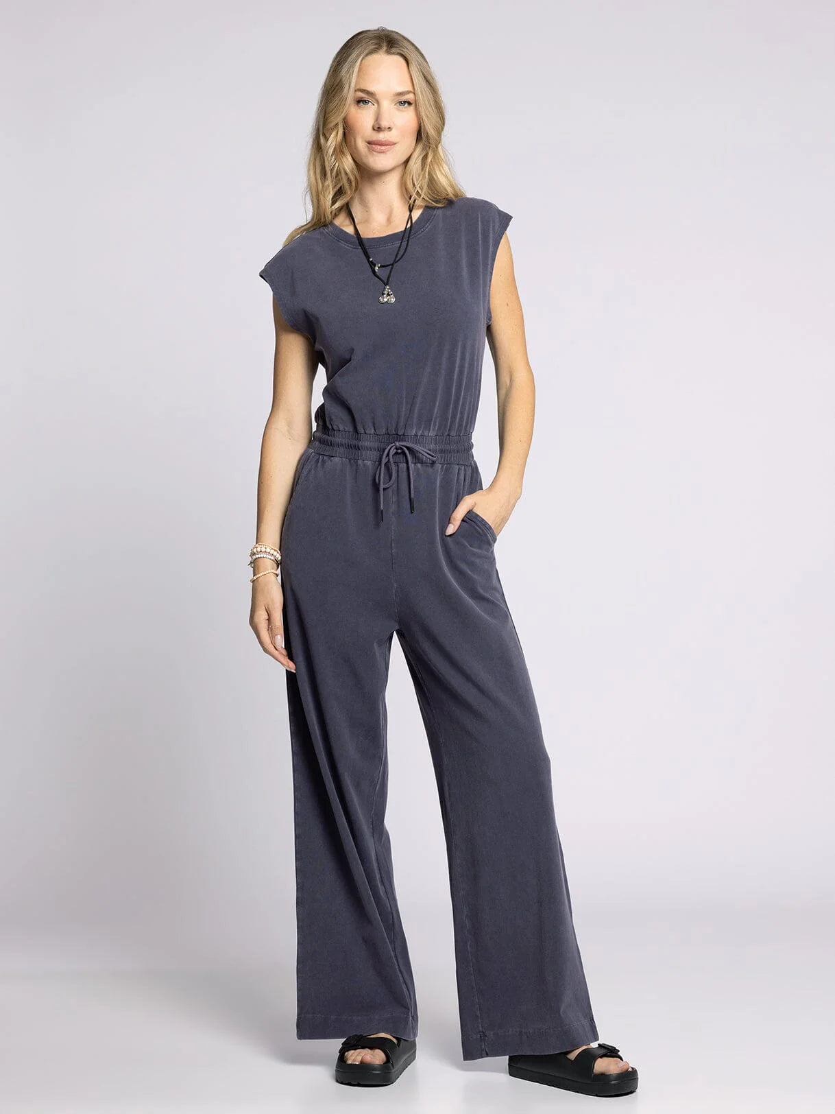 Woman wearing a dark gray jumpsuit on a light gray background