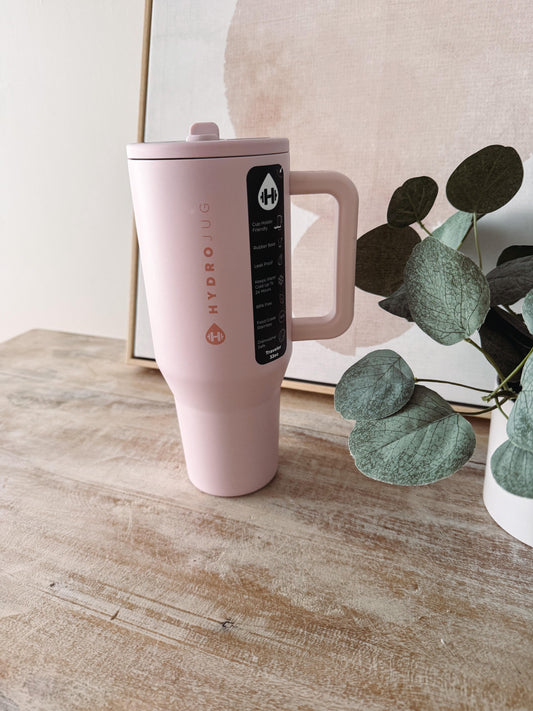 Pink travel mug with a brand logo on a wooden surface with a plant in the background