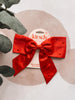 Red satin bow with rhinestones on a 'kit-sch' branded card, surrounded by green leaves.