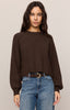 Woman wearing a brown sweater and blue jeans against a plain background