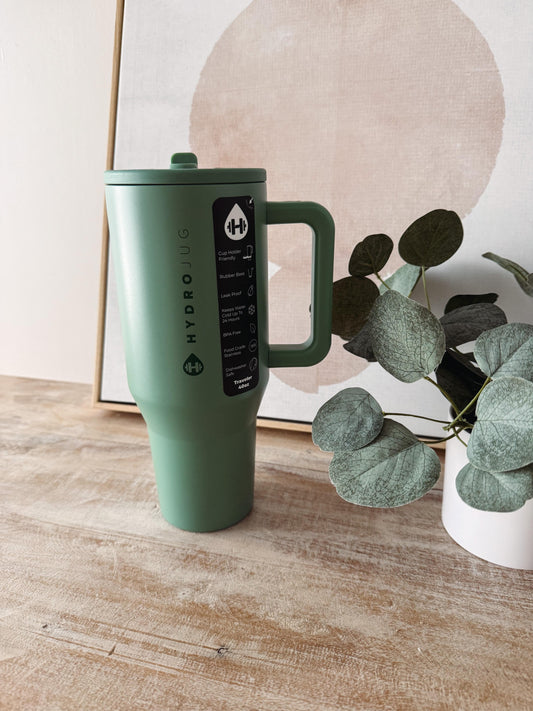 Green Hydroflask mug on a wooden surface with a plant in the background