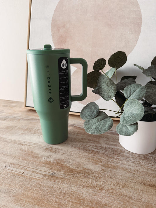Green Hydro Flask mug on a wooden surface with a plant in the background