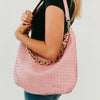 Pink handbag with chain detail held by a person on a plain background