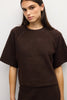 A woman wearing a dark brown short-sleeve knit sweater against a plain light gray background.