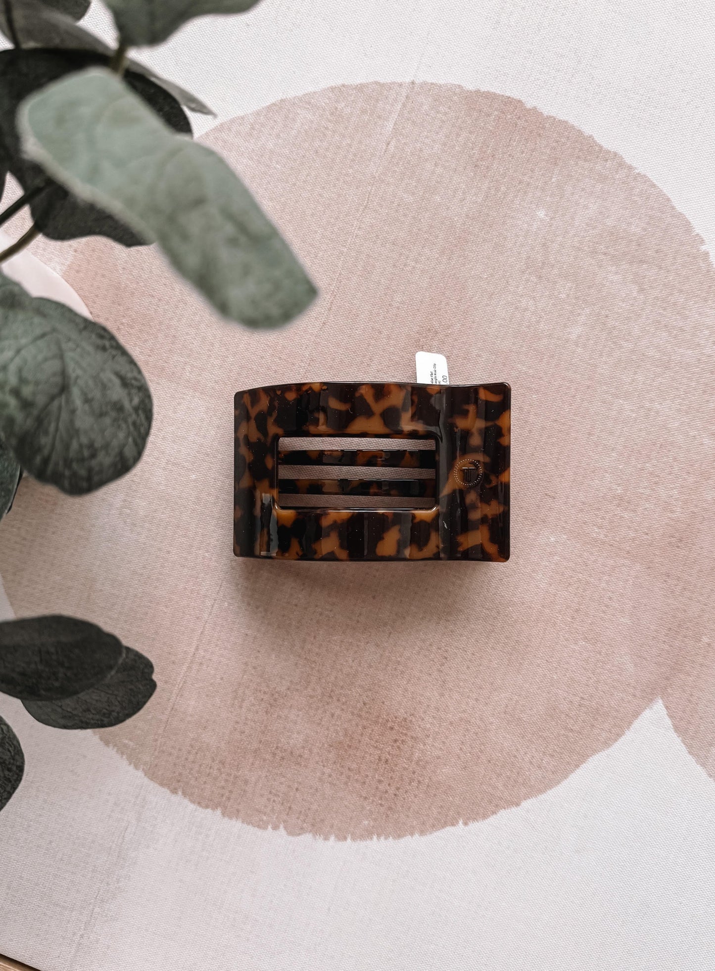 Tortoiseshell hair clip on a pink circular background with green leaves.