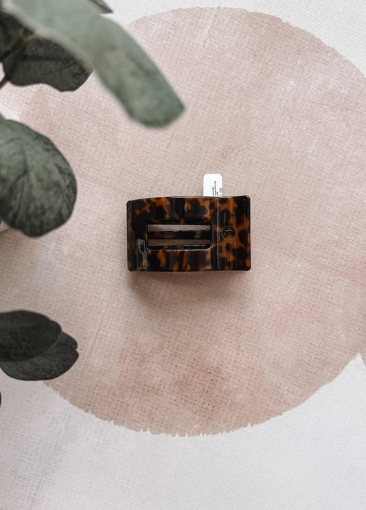 Tortoiseshell hair clip on a beige circular mat with green leaves.