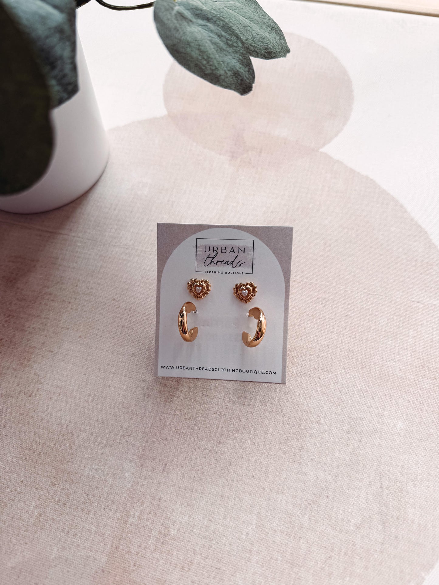 Gold earrings on a card with 'Urban Threads' branding on a light fabric background