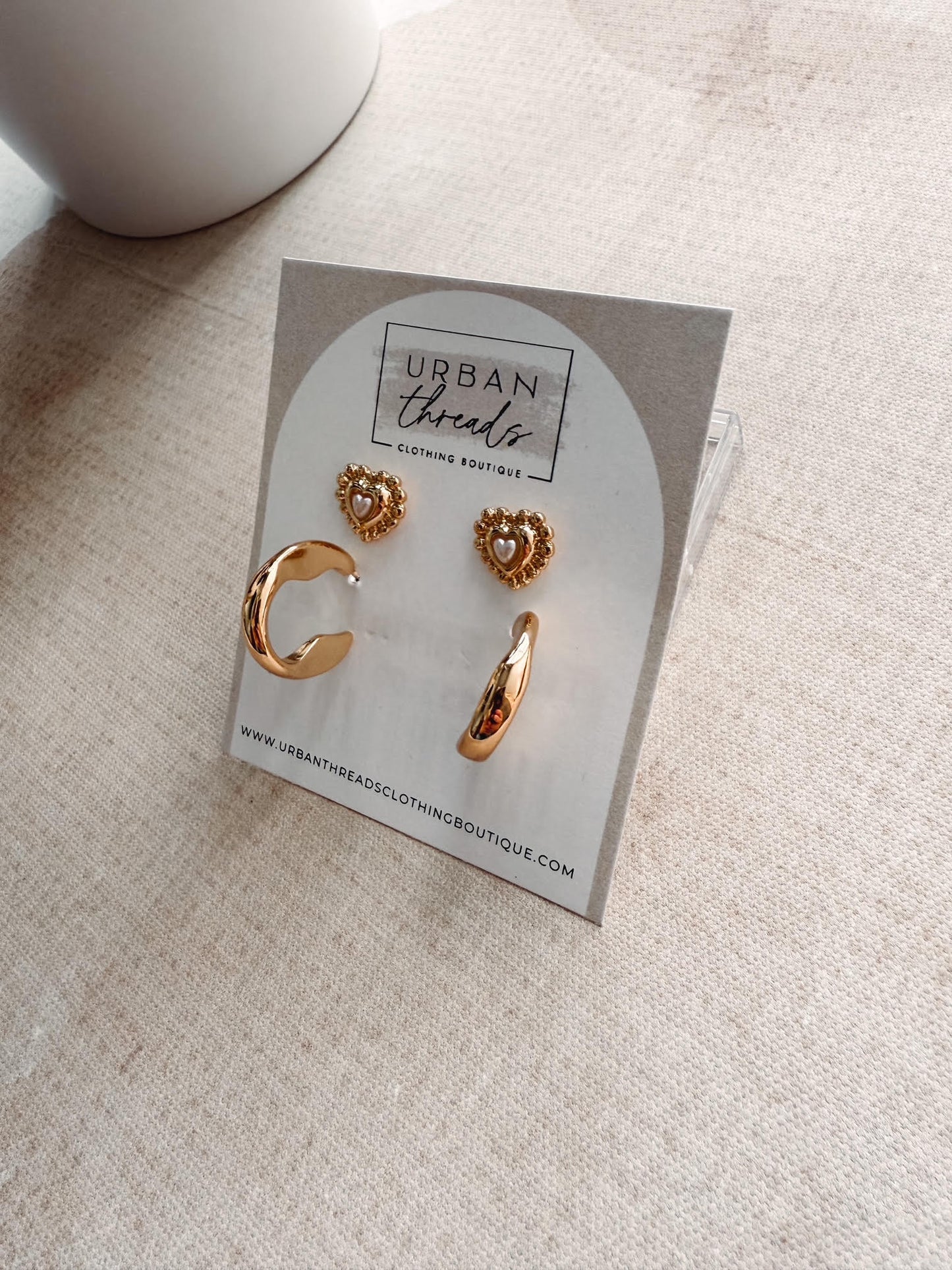 Gold heart-shaped earrings on a 'Urban Threads' branded card on a beige surface.
