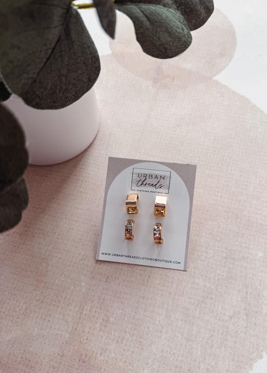 Set of gold earrings on a branded card with a blurred plant in the background