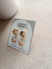 Gold earrings on a branded card with 'Urban Threads' on a beige surface