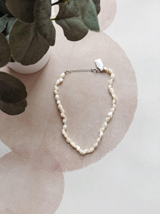 Pearl necklace on a decorative surface with a plant in the background