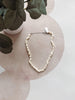 Pearl necklace on a decorative surface with a plant in the background