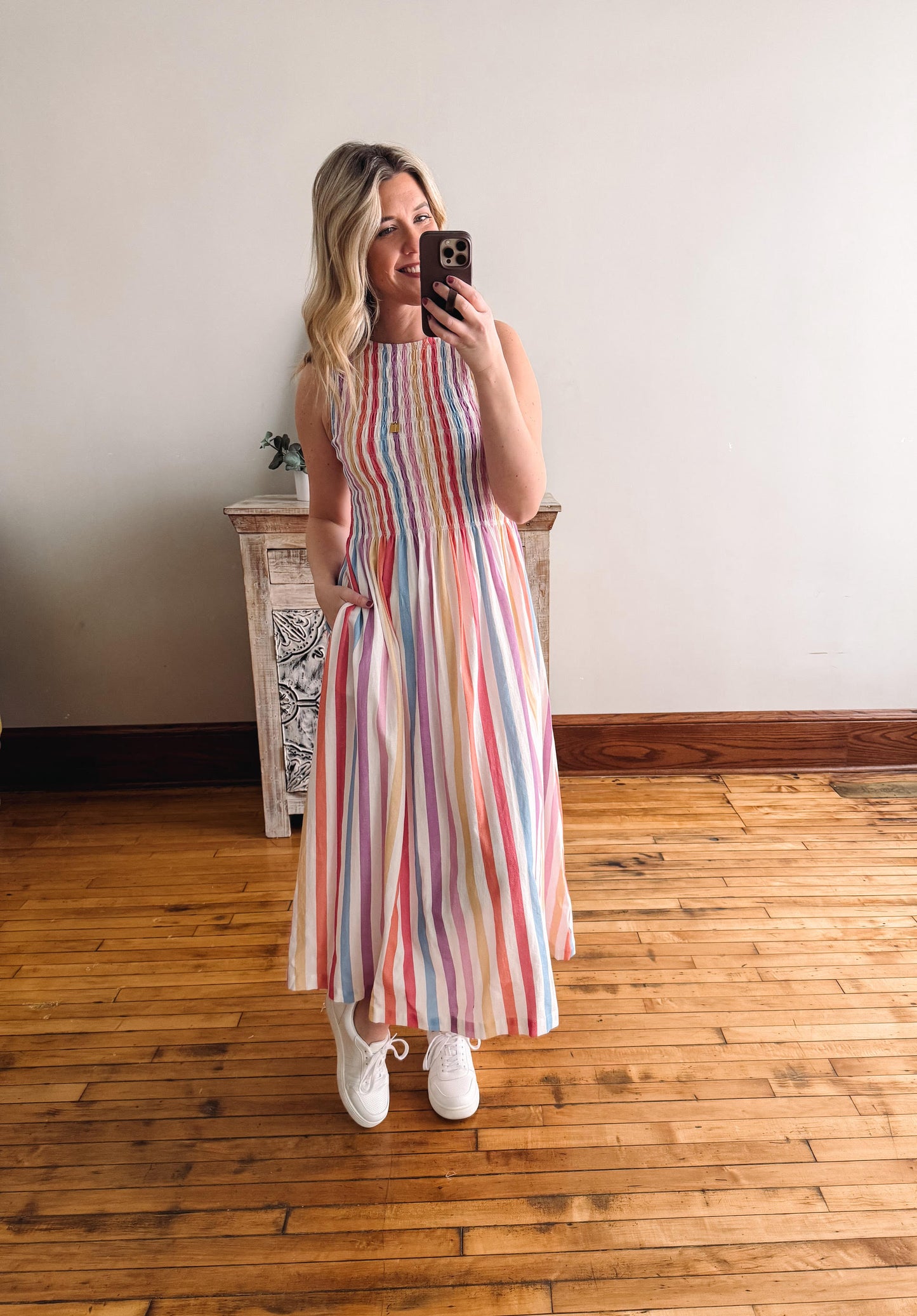 Woman taking a mirror selfie wearing a colorful striped dress in a room with wooden flooring.
