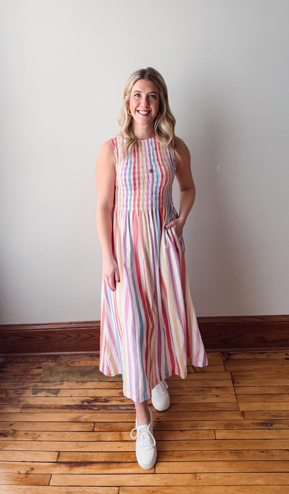 Woman wearing a striped dress standing on a wooden floor with a white wall background