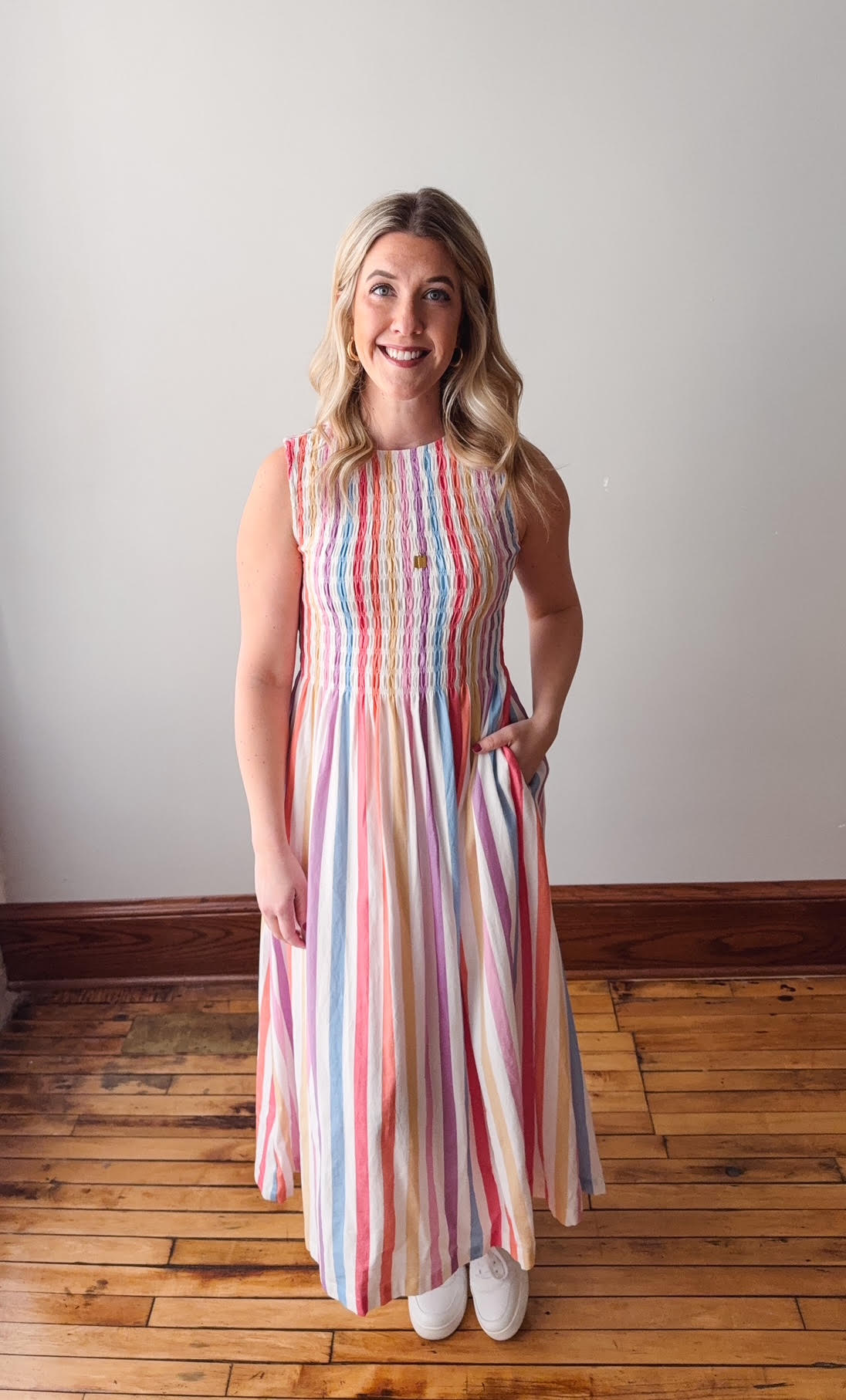 Woman wearing a colorful striped dress standing on a wooden floor with a white wall background
