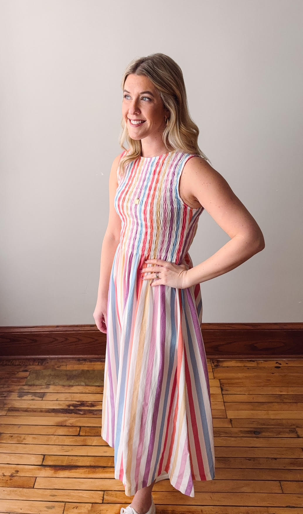 Woman wearing a colorful striped dress standing on a wooden floor.