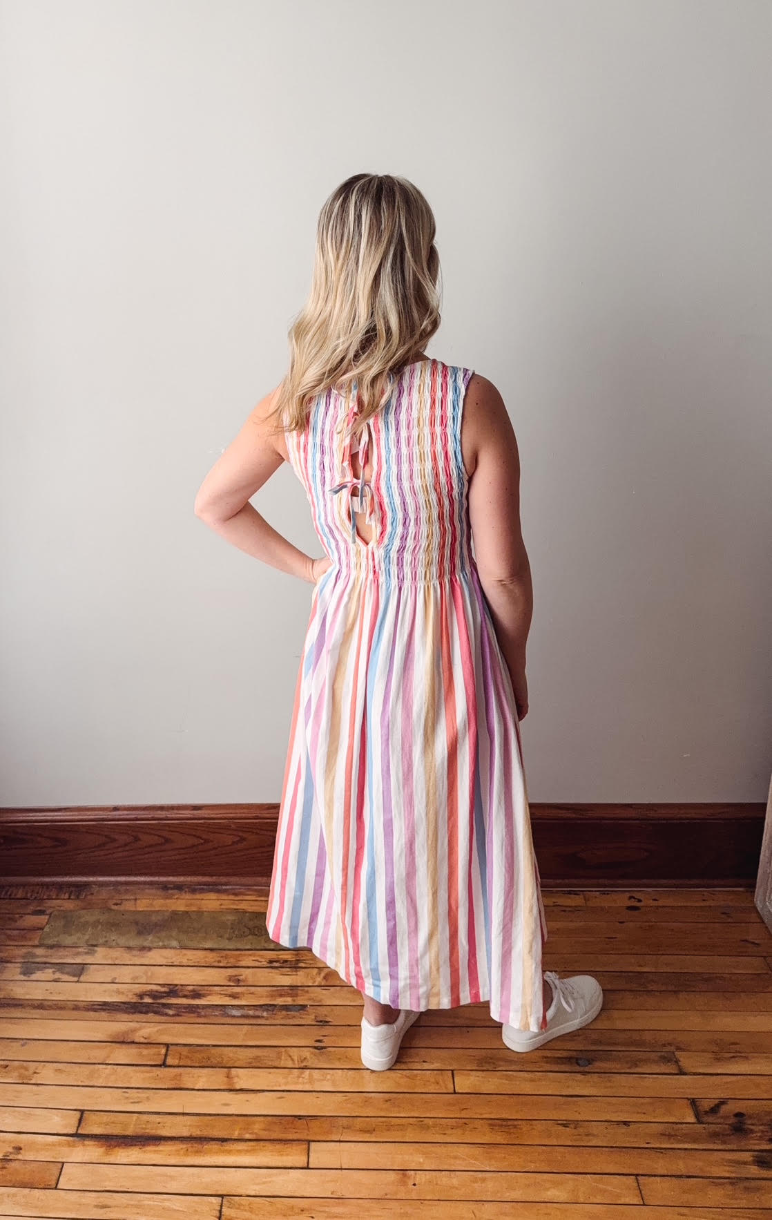 Woman wearing a colorful striped dress standing on a wooden floor with a plain wall background