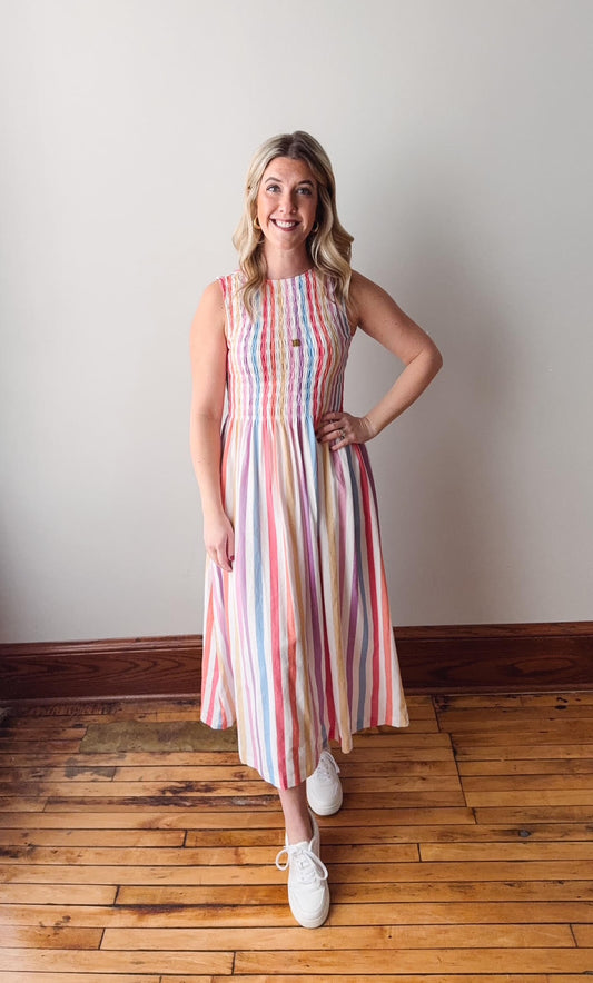 Woman wearing a striped dress standing on a wooden floor against a white wall
