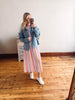 Woman taking a mirror selfie wearing a striped dress, denim jacket, and white sneakers on a wooden floor.
