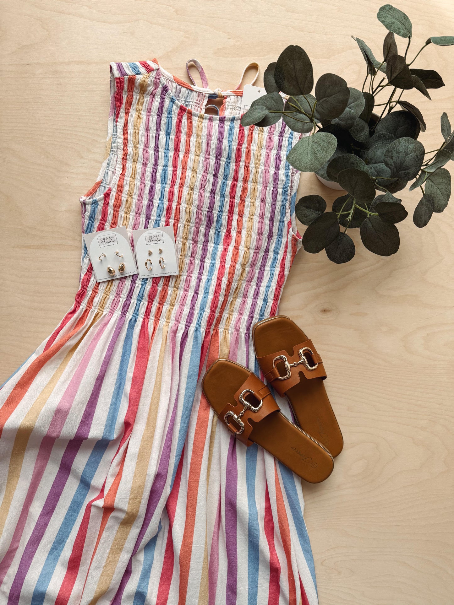 Colorful striped dress with brown sandals and a plant on a wooden surface