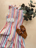 Colorful striped dress with brown sandals and a plant on a wooden surface