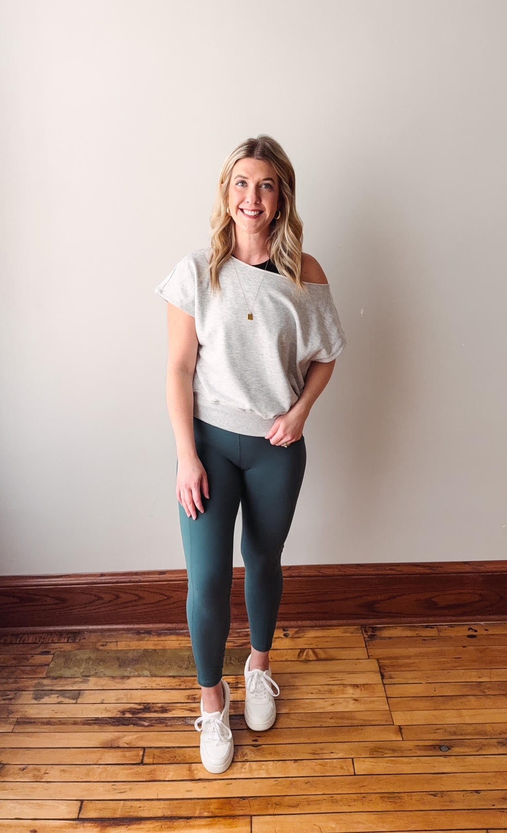 Woman wearing a white oversized shirt and green leggings standing on a wooden floor.