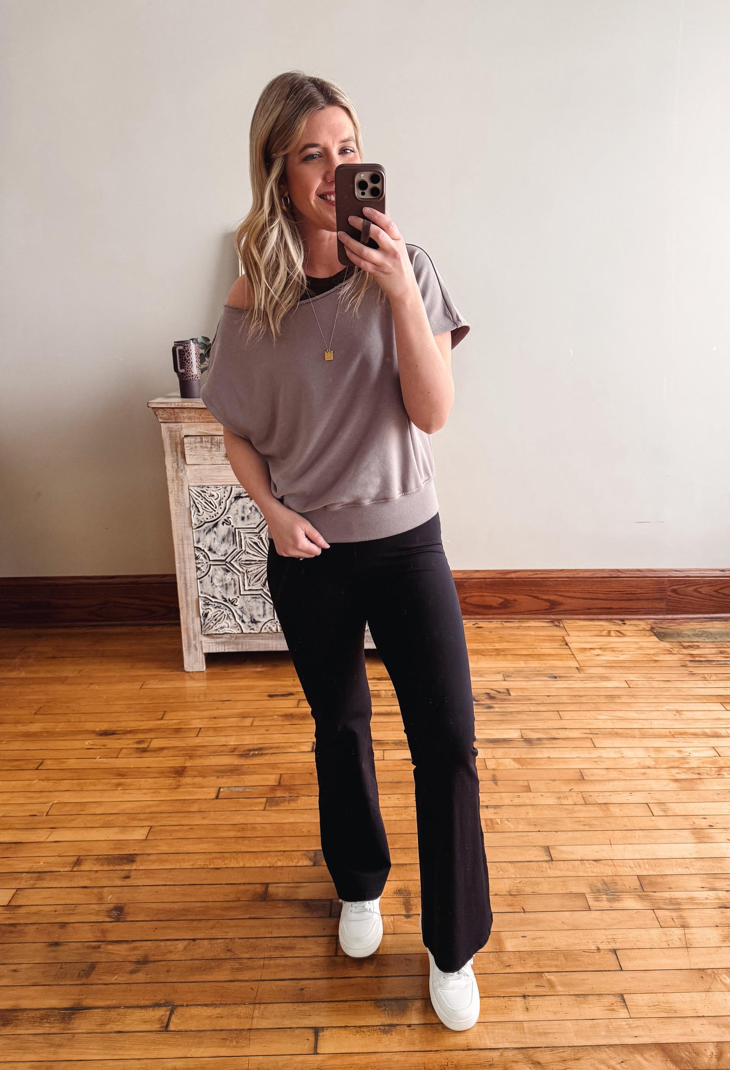 Woman taking a mirror selfie wearing a gray oversized t-shirt and black pants on a wooden floor.