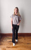 Woman wearing a gray t-shirt and black pants standing on a wooden floor with a white wall background