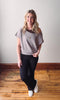 Woman wearing a gray off-shoulder top and black leggings on a wooden floor.