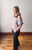 Woman wearing a gray off-shoulder top and black pants standing on a wooden floor.