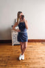 Woman taking a mirror selfie wearing a blue dress and white sneakers in a room with wooden flooring.