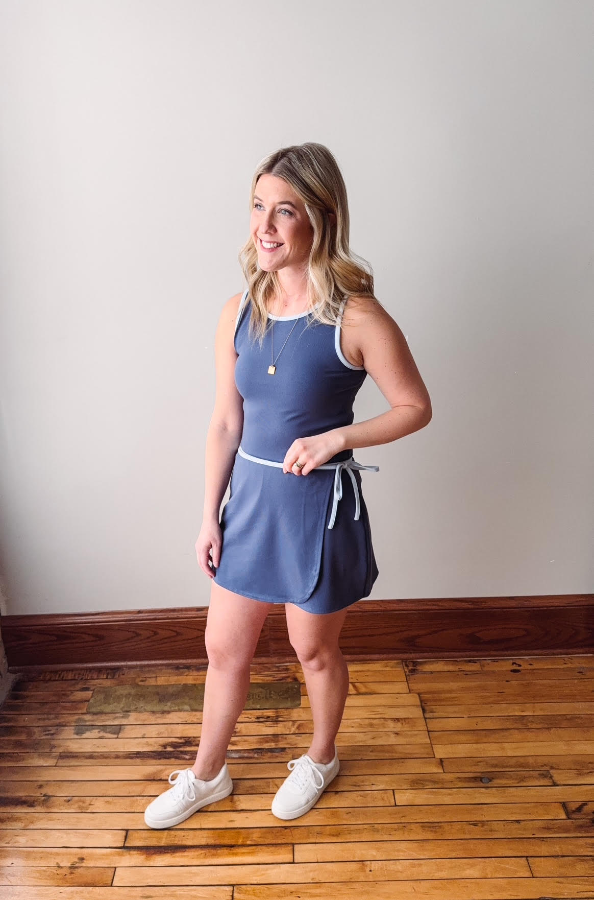 Woman wearing a blue dress standing on a wooden floor with a white wall background