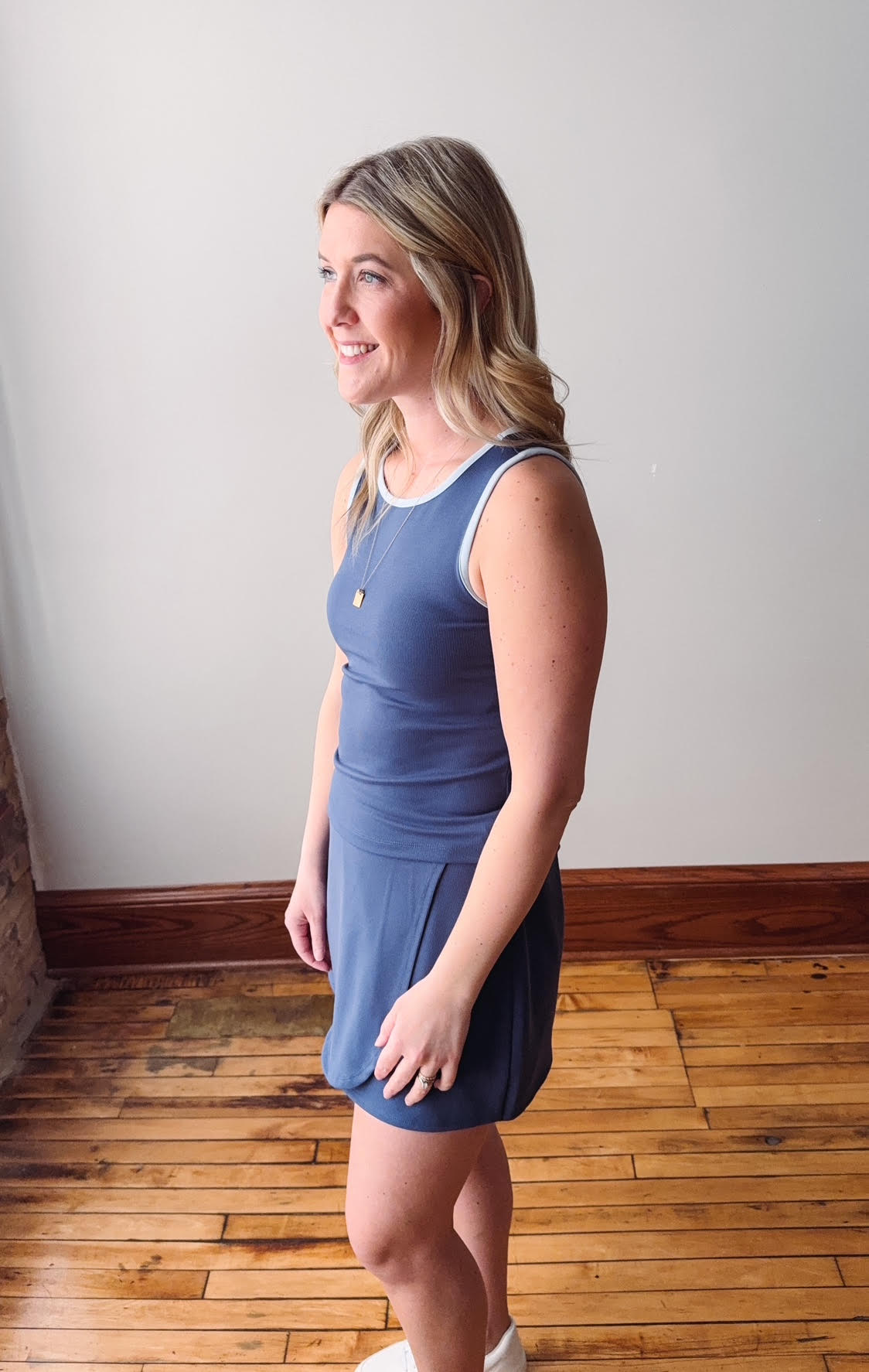 Woman wearing a blue dress standing on a wooden floor with a white wall background