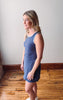 Woman wearing a blue dress standing on a wooden floor with a white wall background