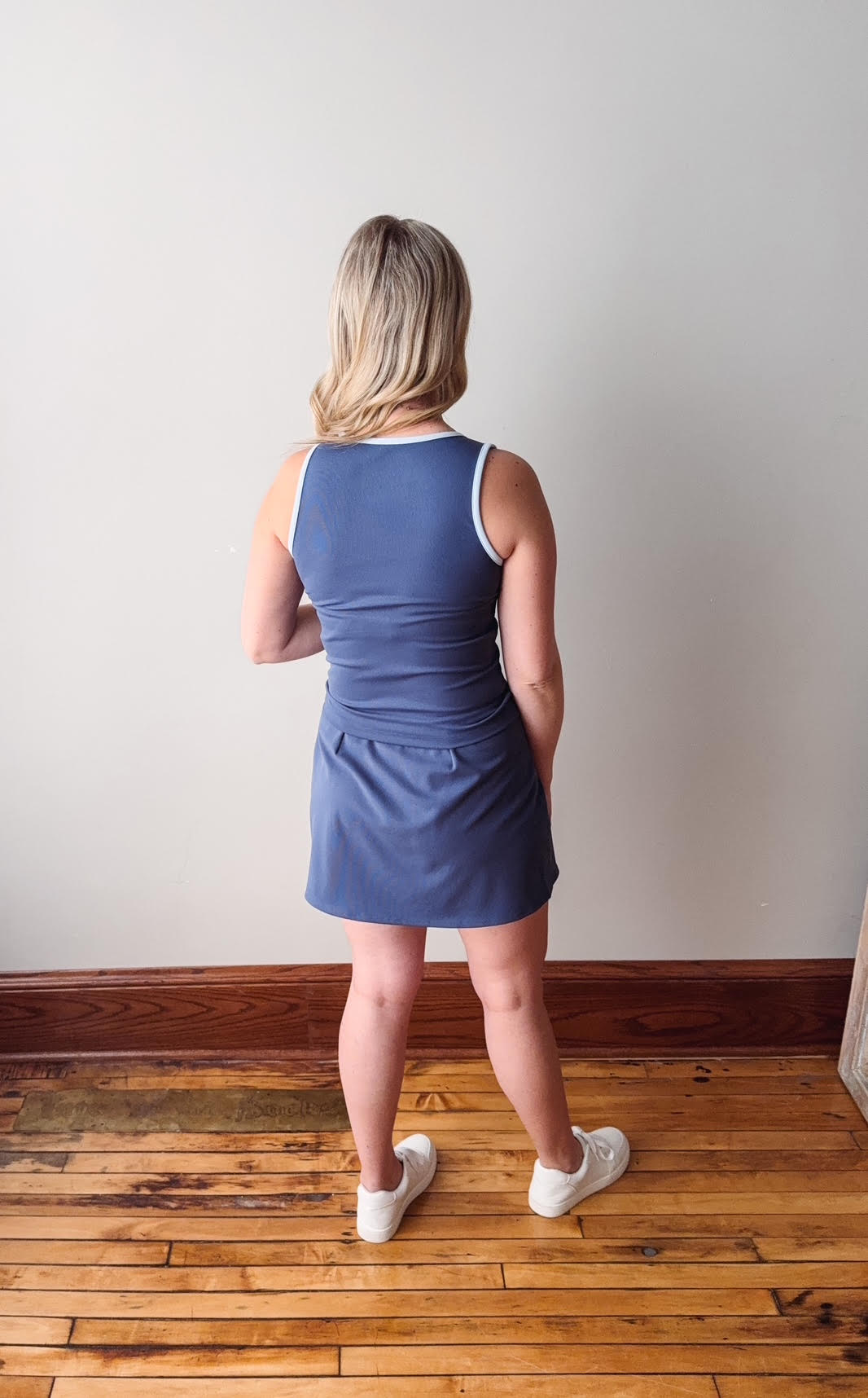 Woman wearing a blue dress standing on a wooden floor with a white wall background