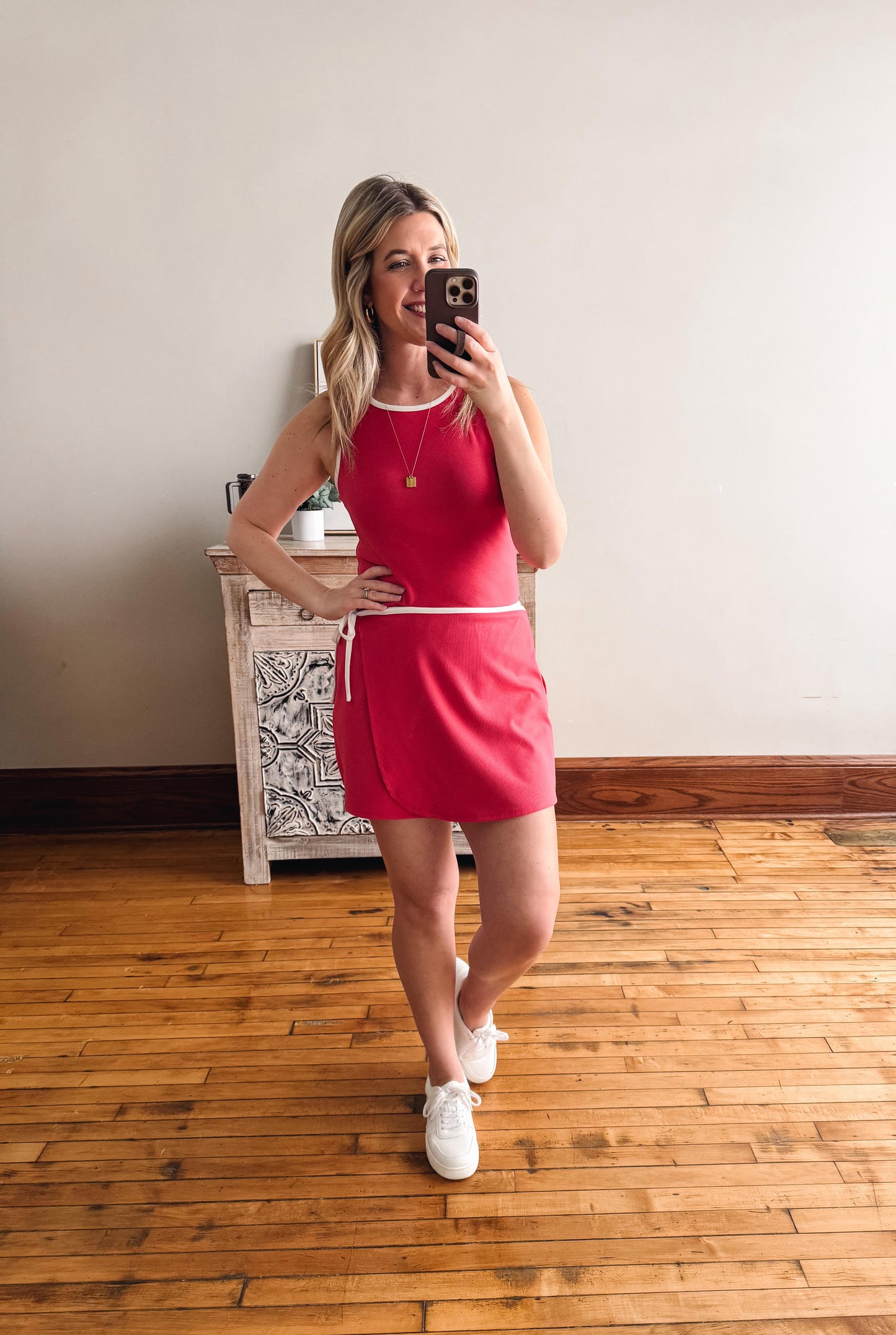 Woman taking a mirror selfie wearing a red dress in a room with wooden flooring.