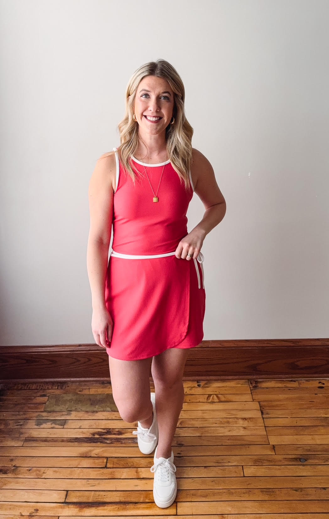 Woman wearing a red dress standing on a wooden floor with a white wall background