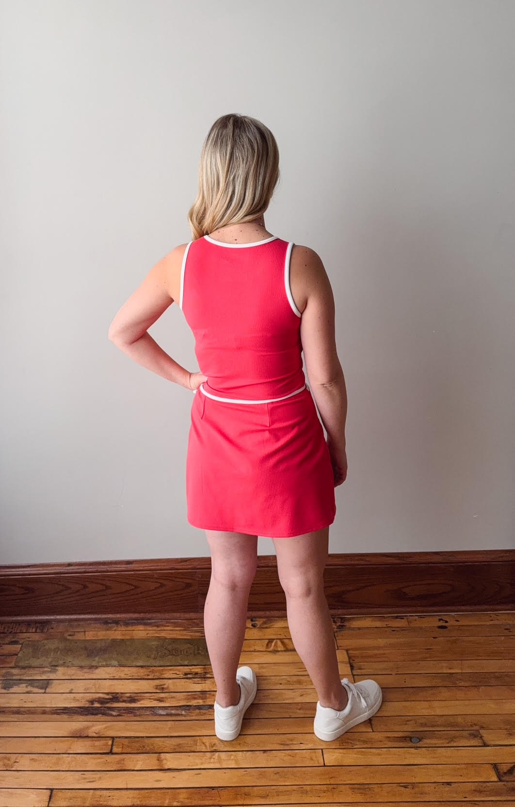 Person wearing a red dress standing on a wooden floor with a plain wall background