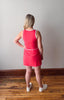 Person wearing a red dress standing on a wooden floor with a plain wall background