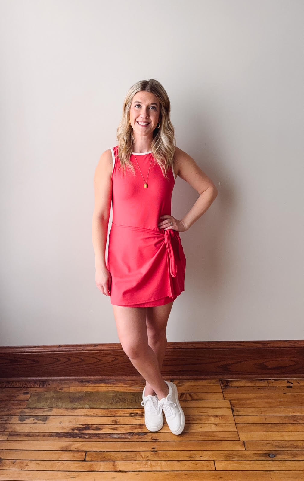 Woman in a red dress standing against a plain wall on a wooden floor