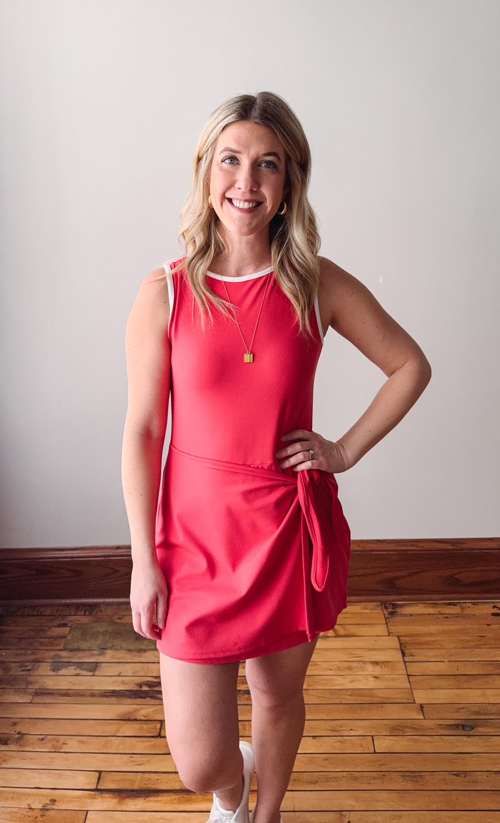 Woman wearing a red dress standing on a wooden floor with a white wall background
