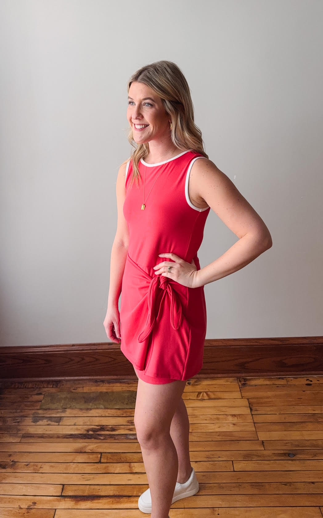 Woman wearing a red dress standing on a wooden floor with a plain wall background