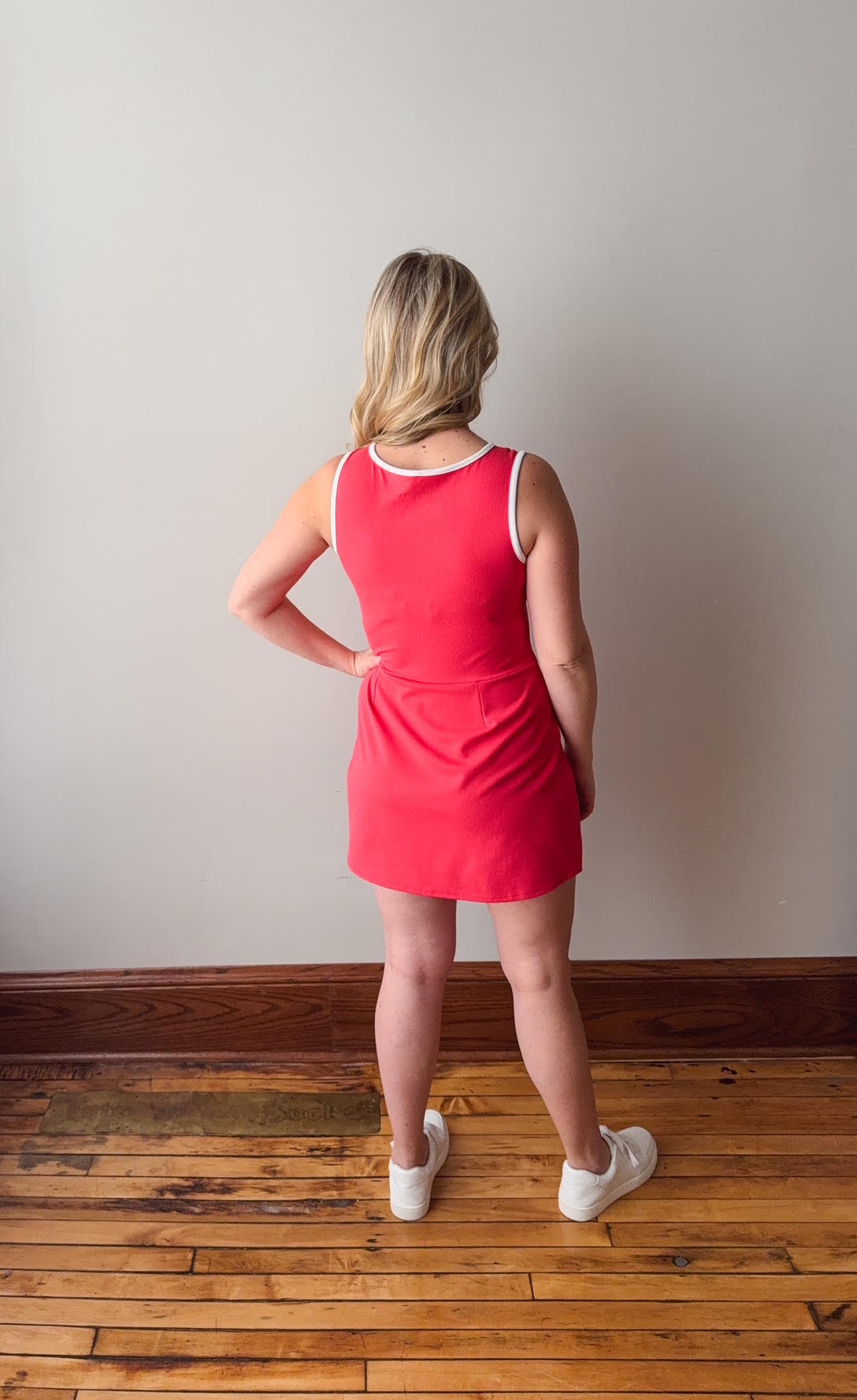 Woman wearing a red dress standing on a wooden floor with a plain wall background