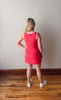 Woman wearing a red dress standing on a wooden floor with a plain wall background