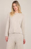 A woman modeling a light beige cable-knit sweater and matching knit pants against a plain light beige studio background.