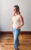 Woman wearing a sleeveless top and jeans standing on a wooden floor with a white wall background